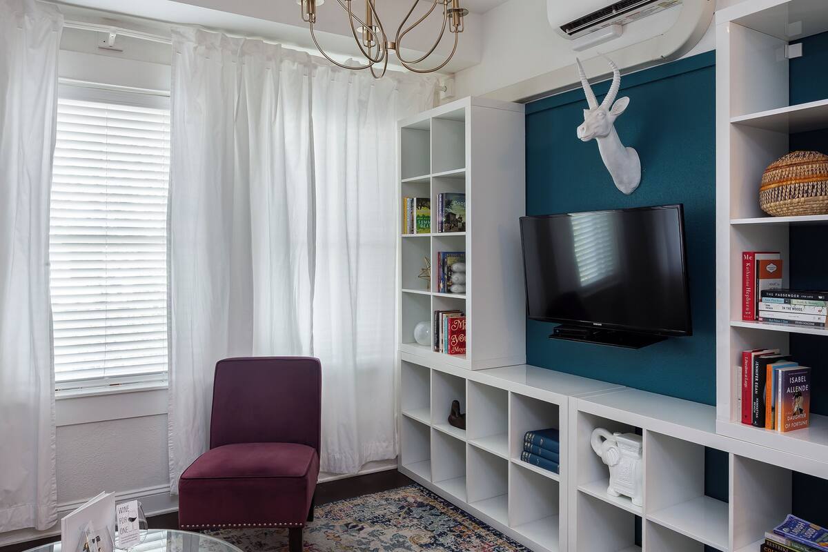A living room with a chandelier, a television, a bookshelf, a red chair, and a patterned rug.