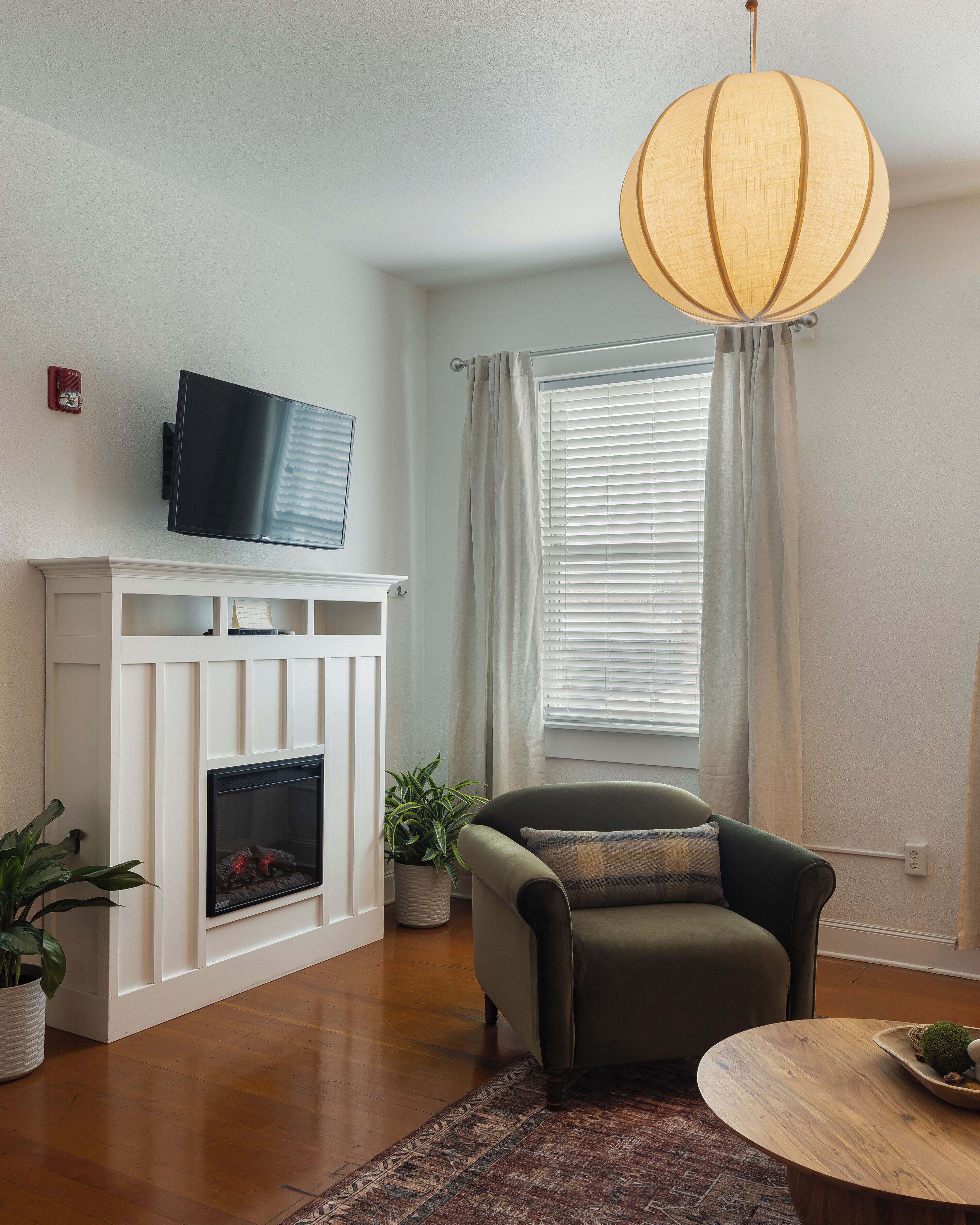 A living room with a fireplace, a television, a sofa, a table, and a hanging light fixture.