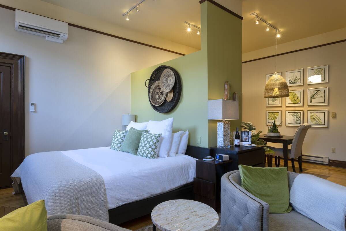 A hotel room with a large bed, a desk with a lamp, a chair, and a round table.
