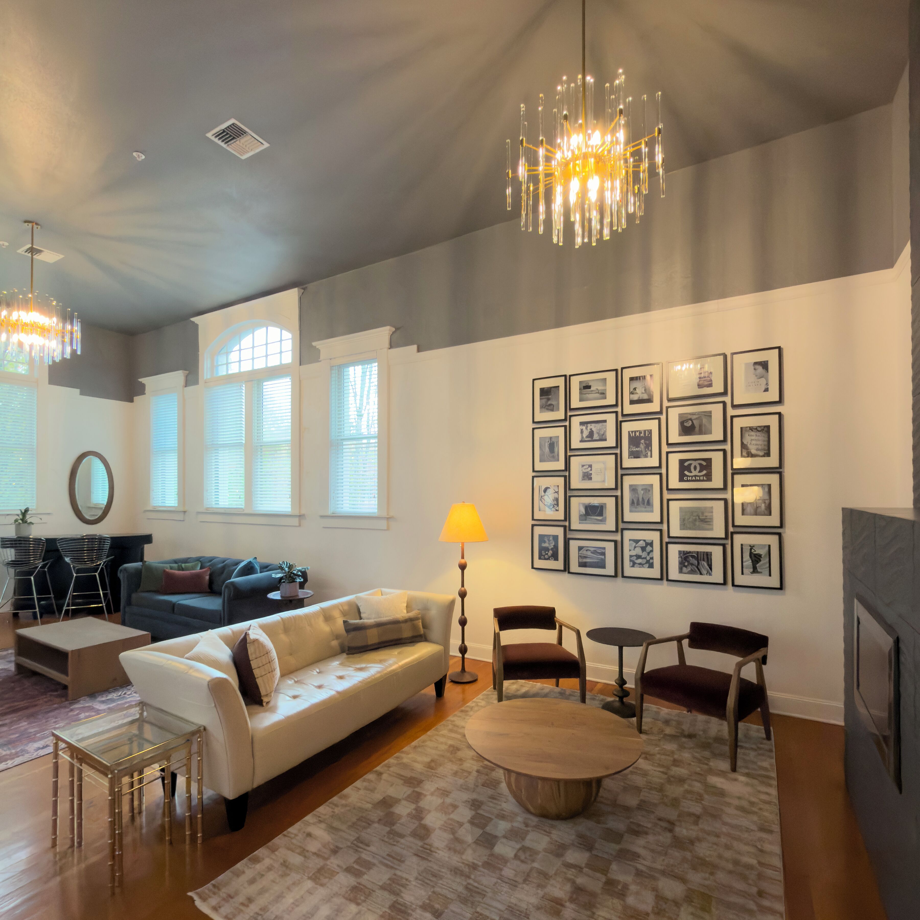 A spacious living room with a chandelier, a fireplace, and a wall of framed pictures.
