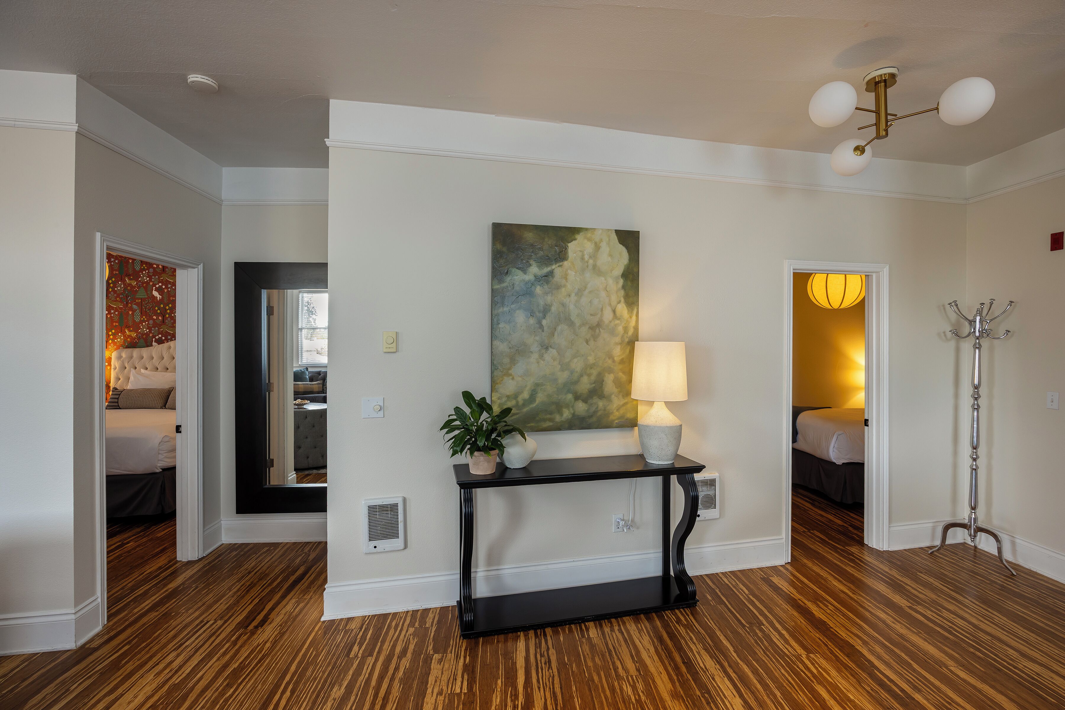 A hotel lobby with a console table, a painting, a lamp, and a coat stand.
