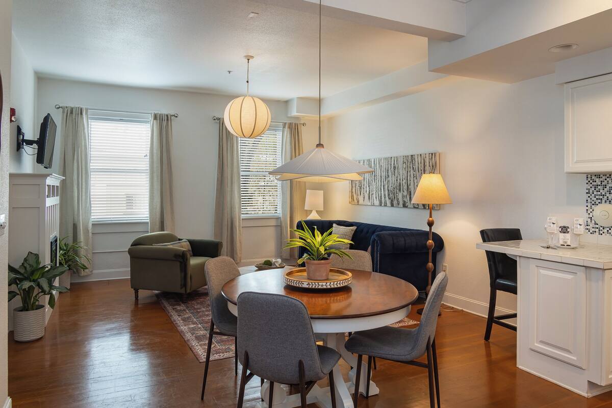 A dining area with a round table, chairs, a potted plant, and a hanging light fixture.
