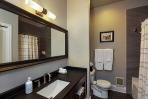 A bathroom with a large mirror, a sink, a toilet, and a shower area. - 3rd Street Flats (McMinnville)