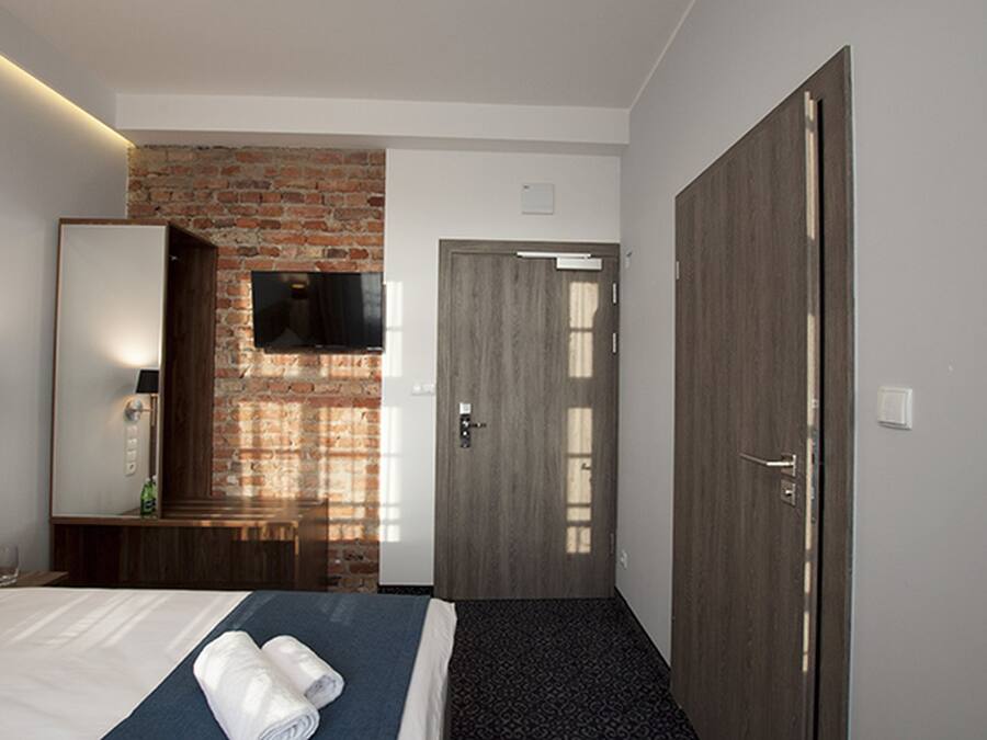 A hotel room with a brick wall, a flat-screen TV, a wooden door, and a bed with a blue bedspread and white linens.