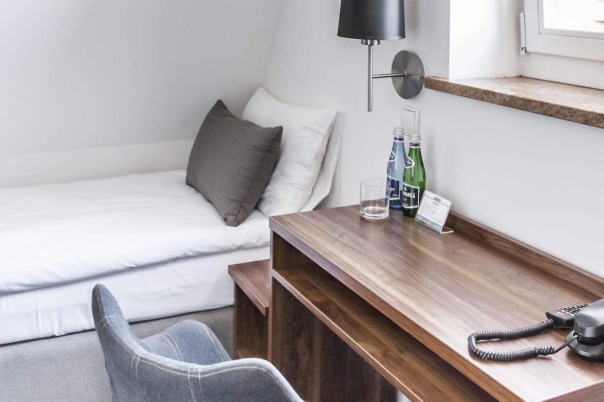 A hotel room with a bed, a desk with a lamp, a chair, and a window with curtains.