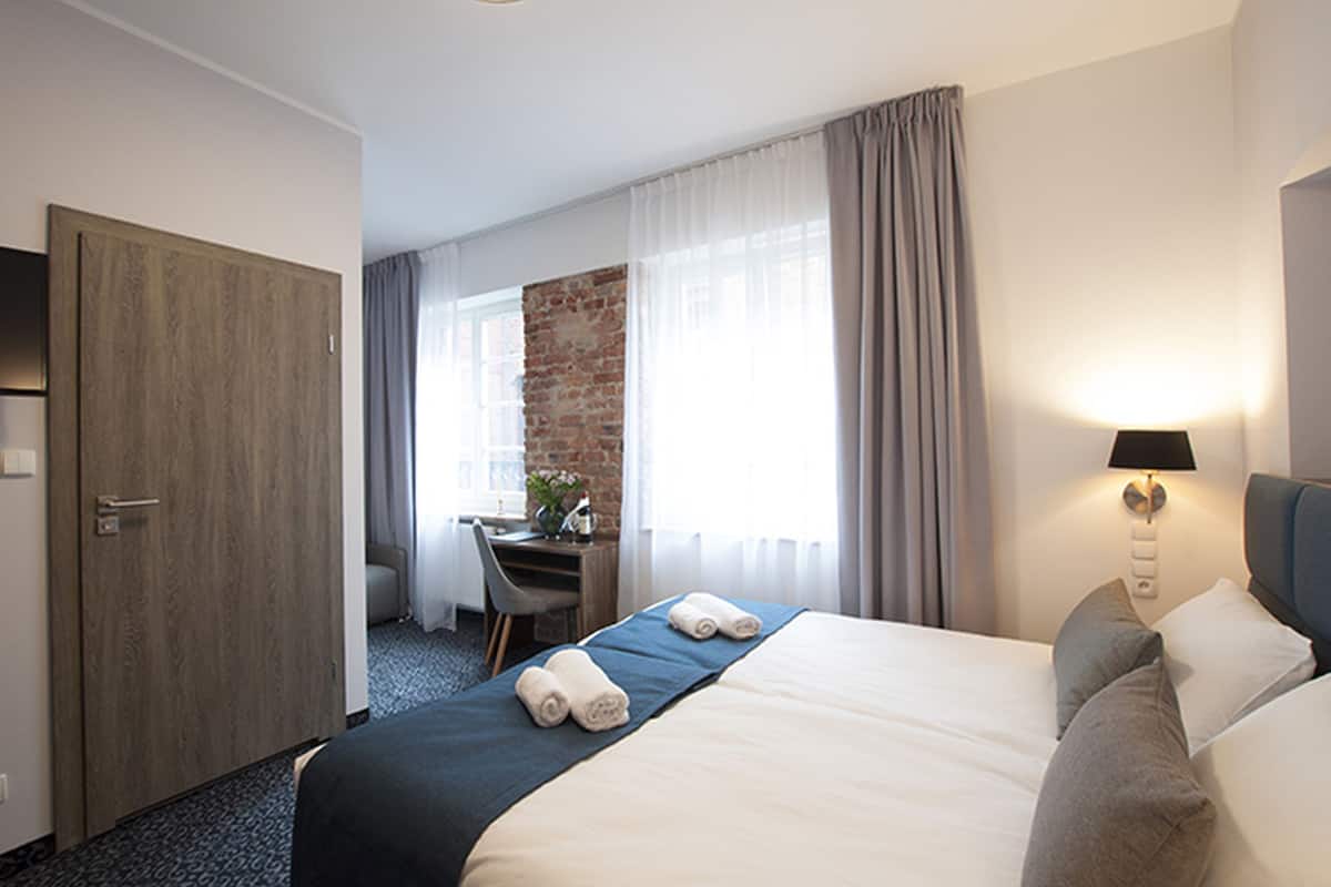 A hotel room with a bed, a desk, a chair, and a lamp.