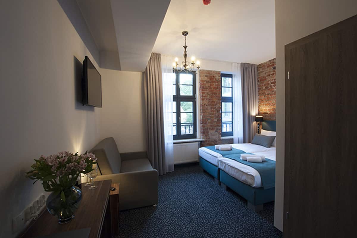 A hotel room with a bed, a desk, a chair, a TV, and a window with curtains.