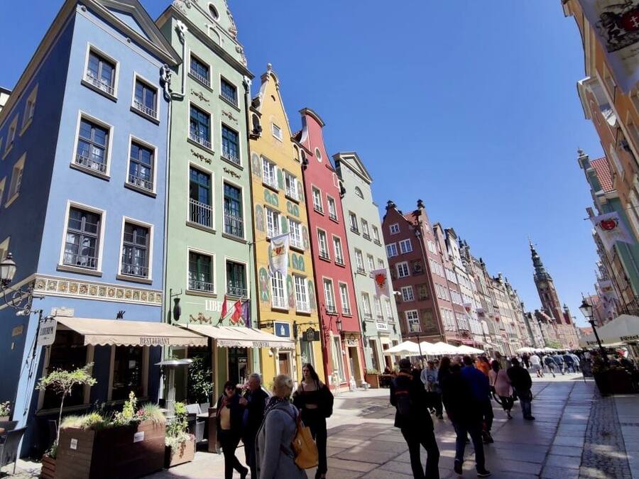 A bustling square with colorful historic buildings, a café, and people walking.