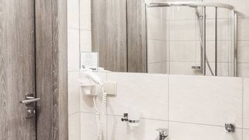 Une salle de bain avec une porte en bois, un lavabo blanc avec des articles de toilette, un miroir et un espace douche.