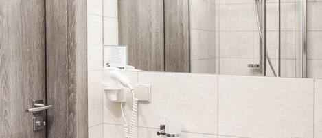 A bathroom with a wooden door, a white sink with toiletries, a mirror, and a shower area.