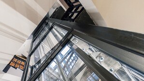 A view through a glass elevator shaft with metal beams and a brick wall. - Liberum Residence (Gdansk)