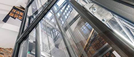 A view through a glass elevator shaft with metal beams and a brick wall.