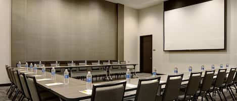A conference room with a long table, chairs, water bottles, a projector screen, and a door.