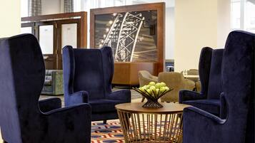 Un vestíbulo de hotel con sillones azul oscuro, una mesa de centro redonda de madera y una alfombra estampada.