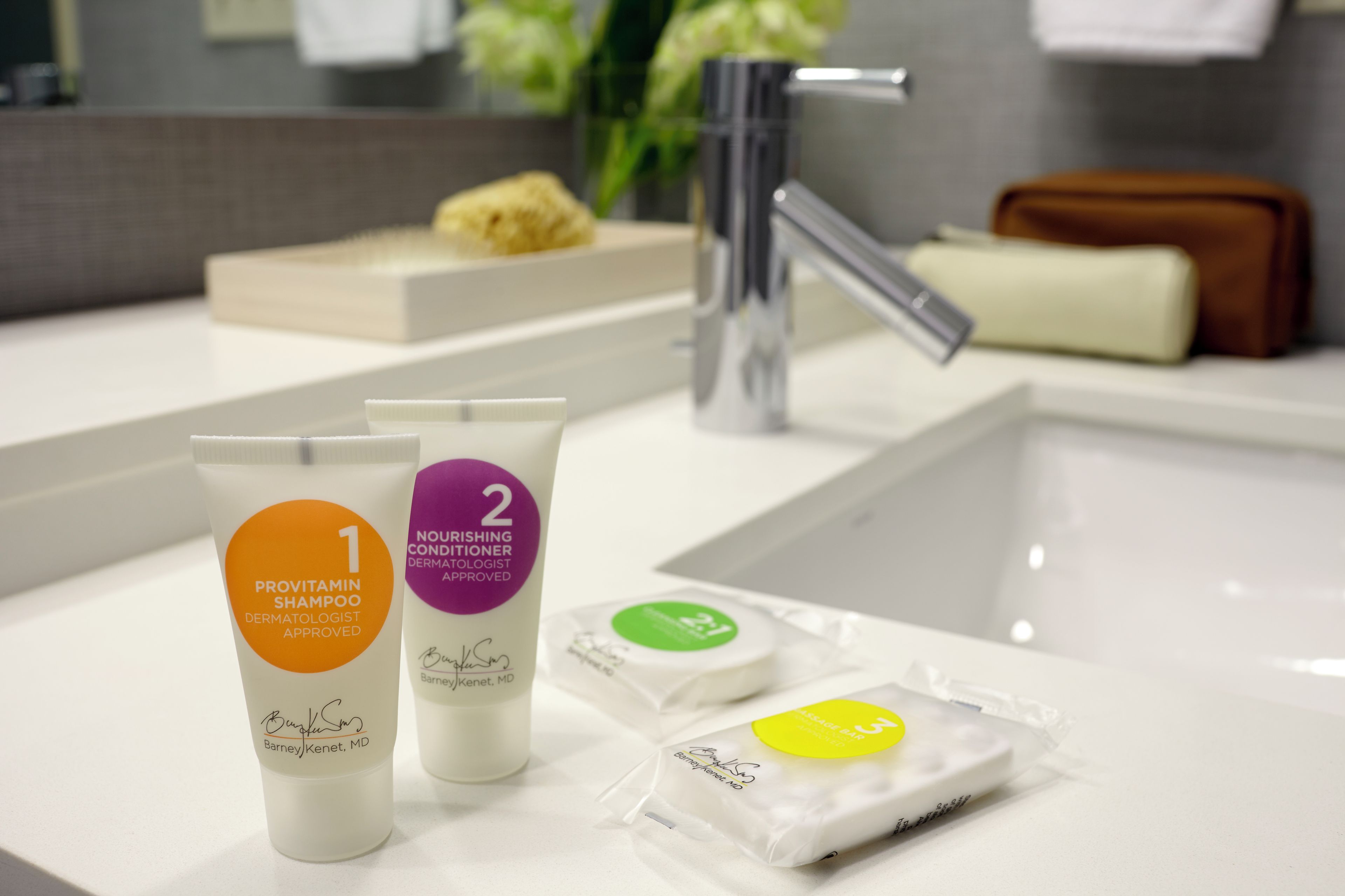 Casa de banho com lavatório branco, dois frascos de produtos de higiene, um sabonete e uma escova de dentes.