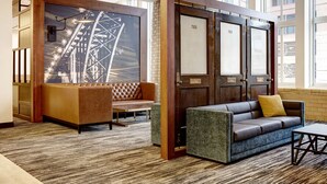 Un vestíbulo con un mostrador de recepción de madera, un sofá y un sillón. Se observan ventanas amplias y una alfombra estampada.
