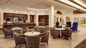Un moderno vestíbulo de hotel con mesas redondas y asientos cómodos, una zona de bar y un diseño espacioso.