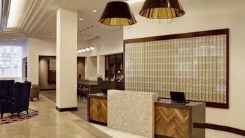 A hotel reception area with a reception desk, seating area, and a large window.