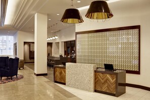 Zona de recepción de hotel con mostrador, área de descanso y un ventanal grande.
