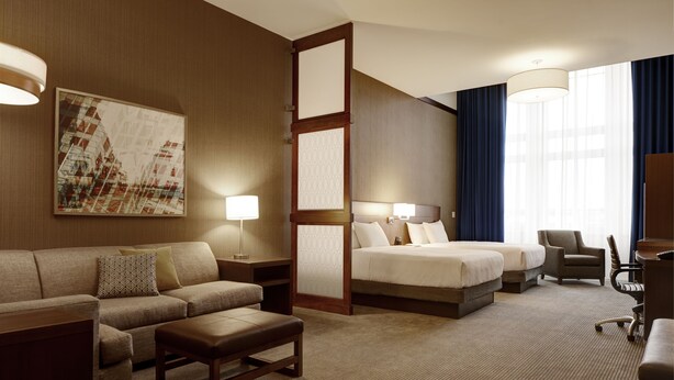 A hotel room with a sofa, two single beds, a desk, and a chair.
