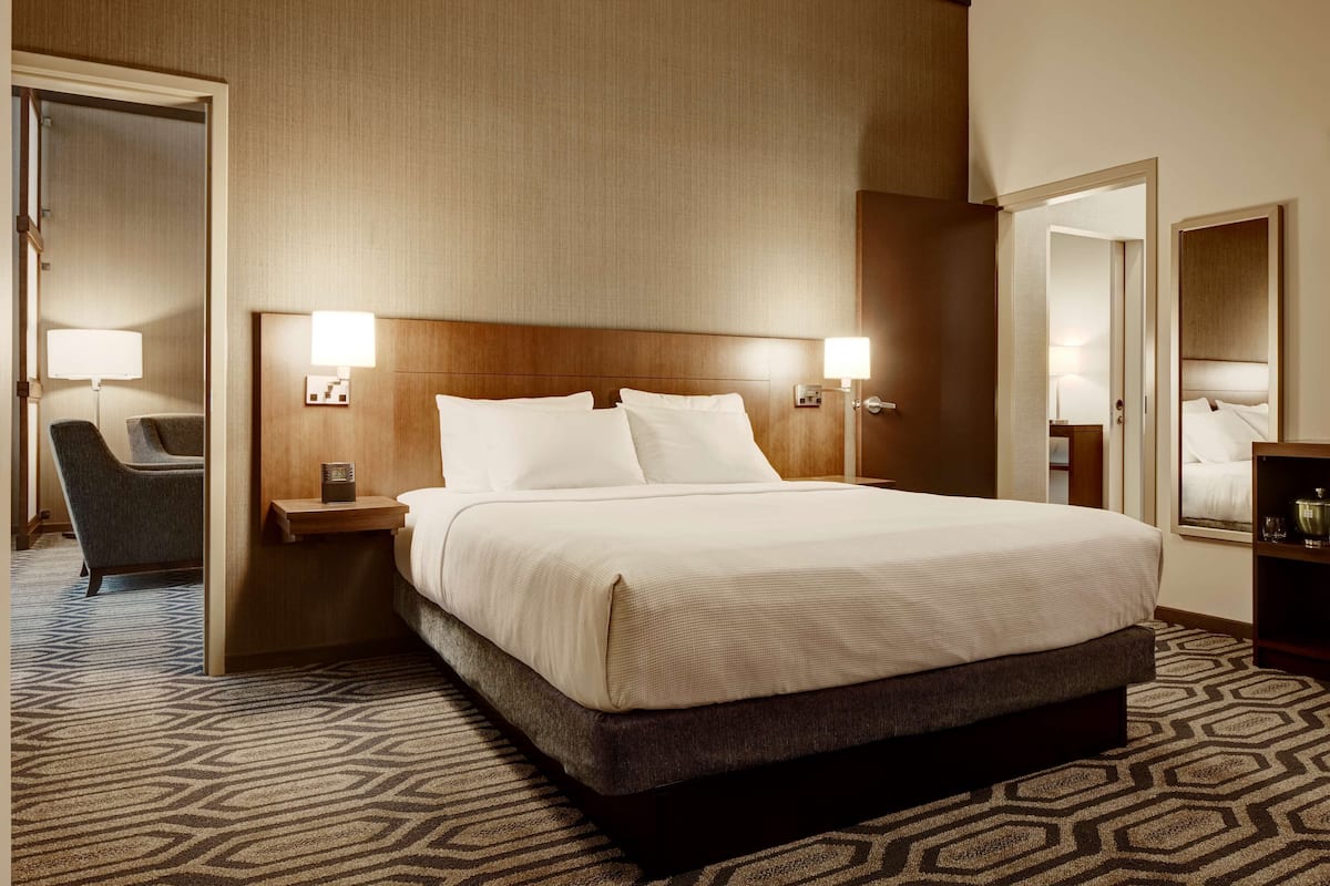 Een hotelkamer met een groot bed, twee nachtkastjes met lampen, een stoel en een spiegel aan de muur.