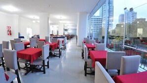 A modern restaurant with red tablecloths and white chairs, large windows with a city view, and a clean, bright interior. - Turis Hotel (Passo Fundo)