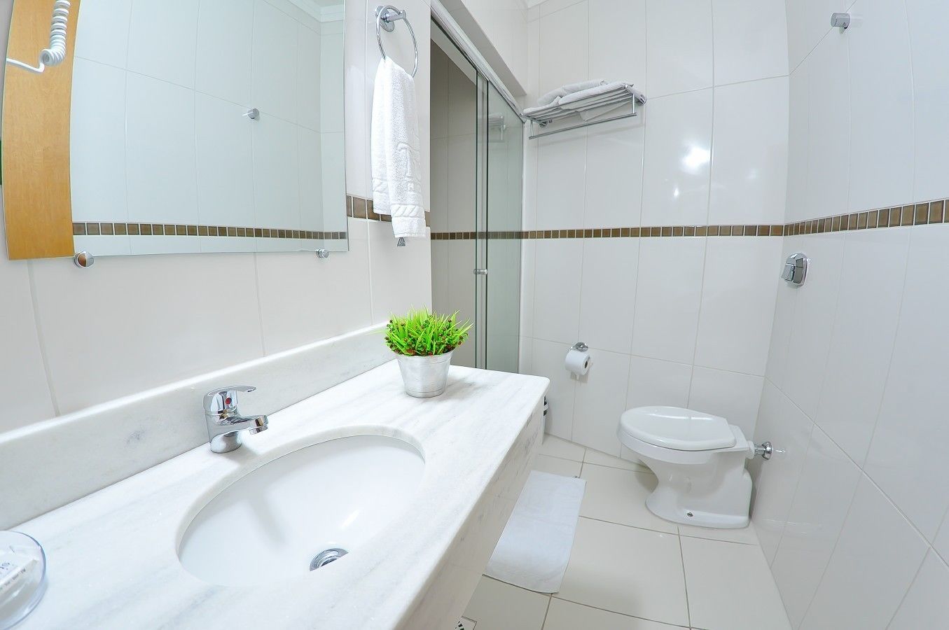 A modern bathroom with a white sink, a toilet, and a small potted plant.