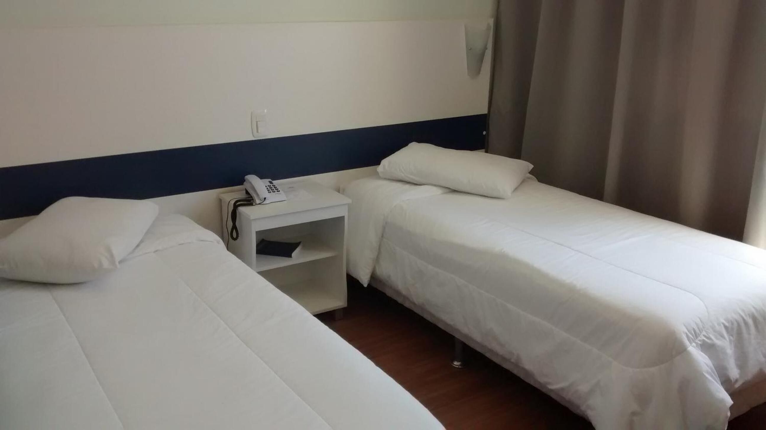 A hotel room with two single beds, a bedside table with a phone, and a wall-mounted light.