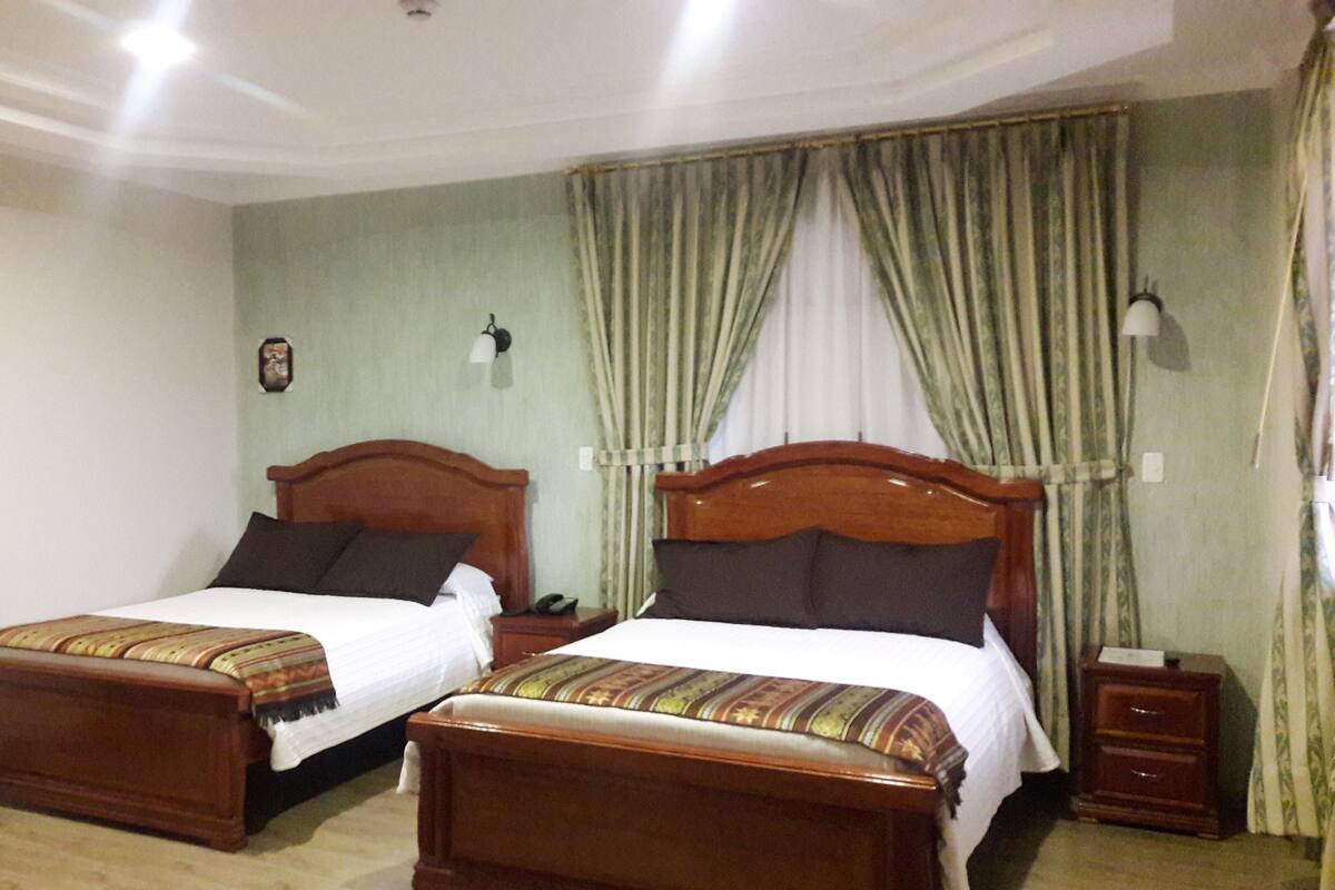 A hotel room with two wooden beds, a nightstand with a lamp, and a framed picture on the wall.