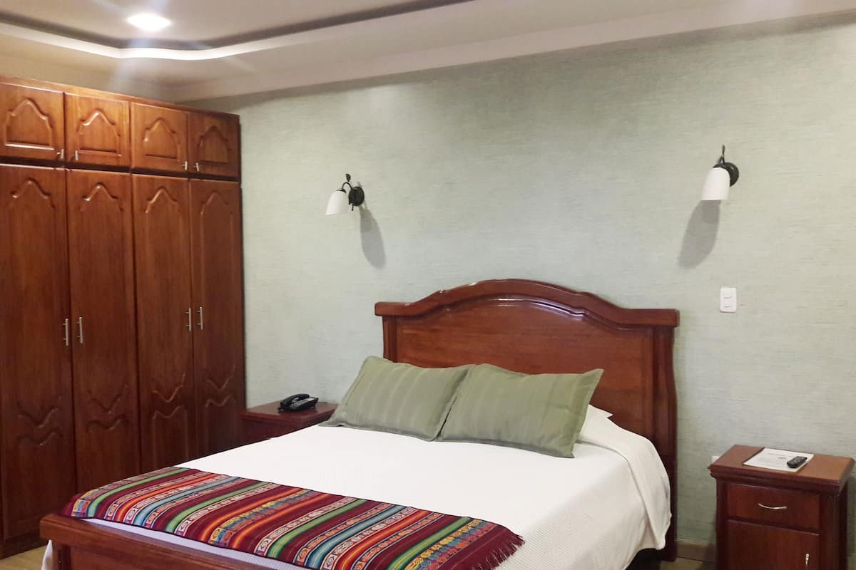 A bedroom with a wooden bed, a nightstand, a wardrobe, and a wall-mounted lamp.
