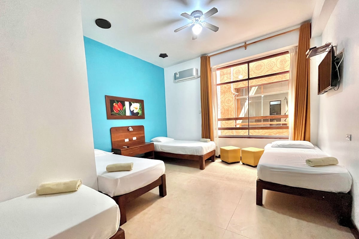 A hotel room with two beds, a ceiling fan, a window with curtains, and a wall-mounted air conditioner.