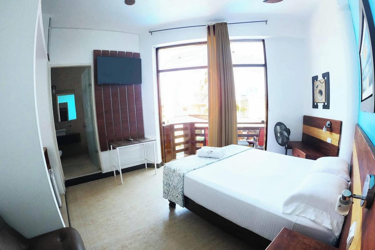 A hotel room with a bed, a desk, a chair, a TV, and a window with curtains.