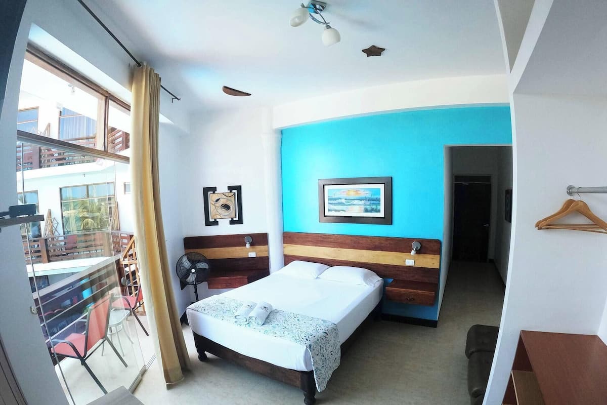 A bedroom with a bed, a fan, a window, and a view of the outside.