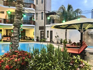 A pool area with lounge chairs, a palm tree, and a building with balconies. - Hotel Aryia (Máncora)
