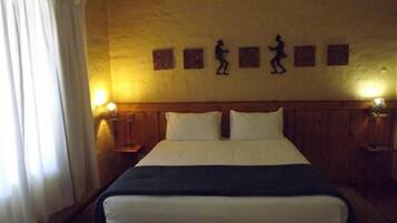 Habitación de hotel con una cama grande, dos mesitas de noche con lámparas, un cabecero de madera y una pared con tres siluetas enmarcadas.