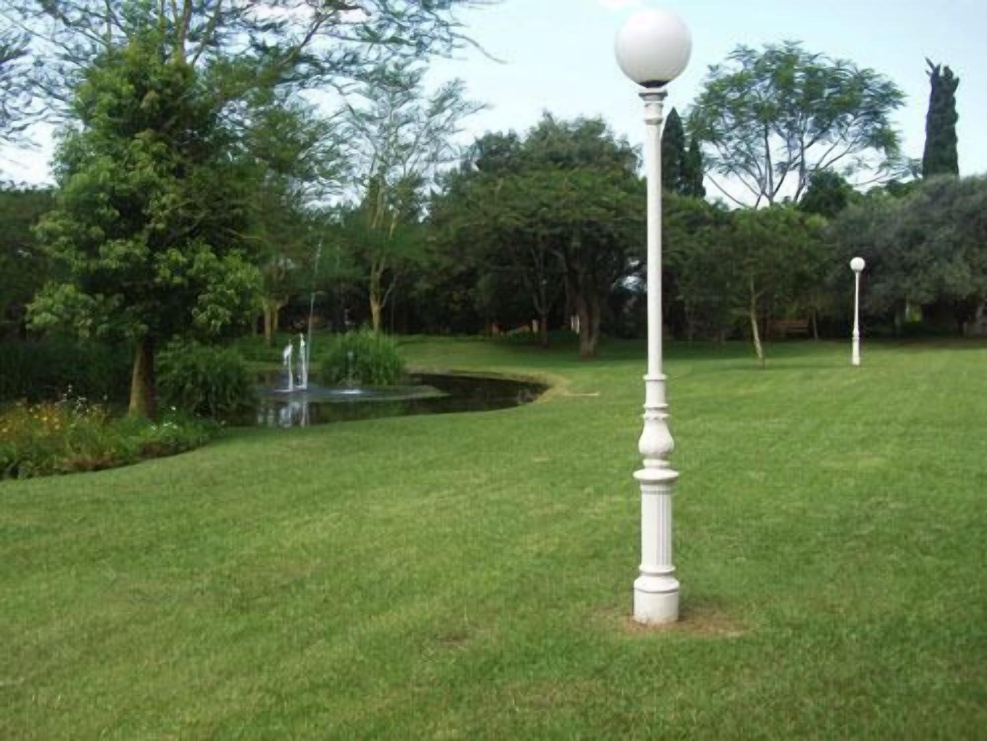 A well-maintained lawn with a white lamp post and a small pond with a fountain.