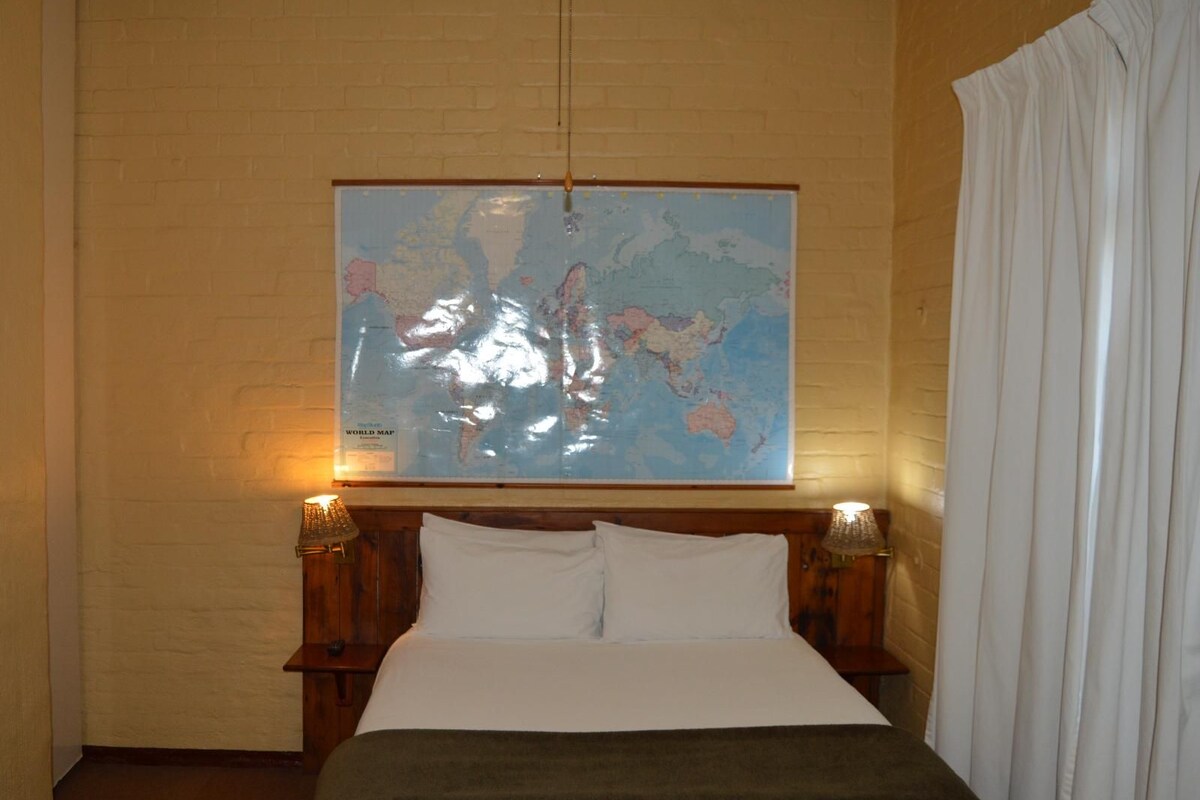 Une chambre à coucher avec une grande carte du monde accrochée au mur, une tête de lit en bois et deux lampes de chevet.