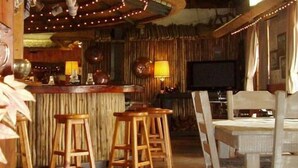 A rustic bar area with wooden stools, a bar counter, and a television. - Ascot Inn (Pietermaritzburg)