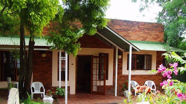 A brick building with a covered porch, white plastic chairs, and potted plants. - Ascot Inn (Pietermaritzburg)