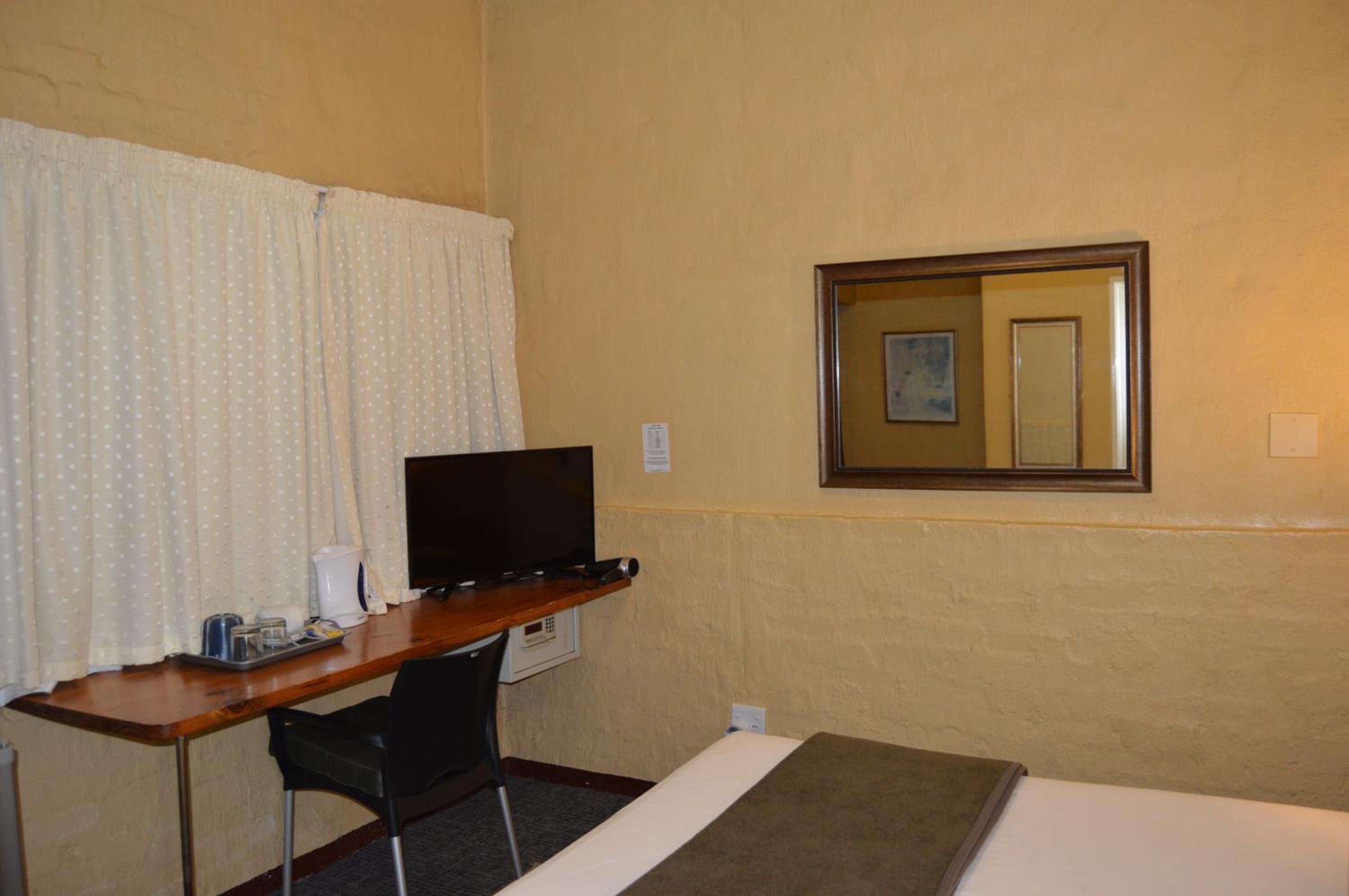 A hotel room with a wooden desk, a television, a chair, a bed, and a mirror on the wall.