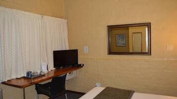 A hotel room with a wooden desk, a television, a chair, a bed, and a mirror on the wall.