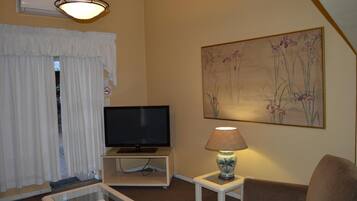 A living room with a television on a stand, a lamp on a side table, and a painting on the wall.