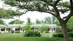A two-story building with a green roof, surrounded by lush greenery and a large tree in the foreground. - Ascot Inn (Pietermaritzburg)