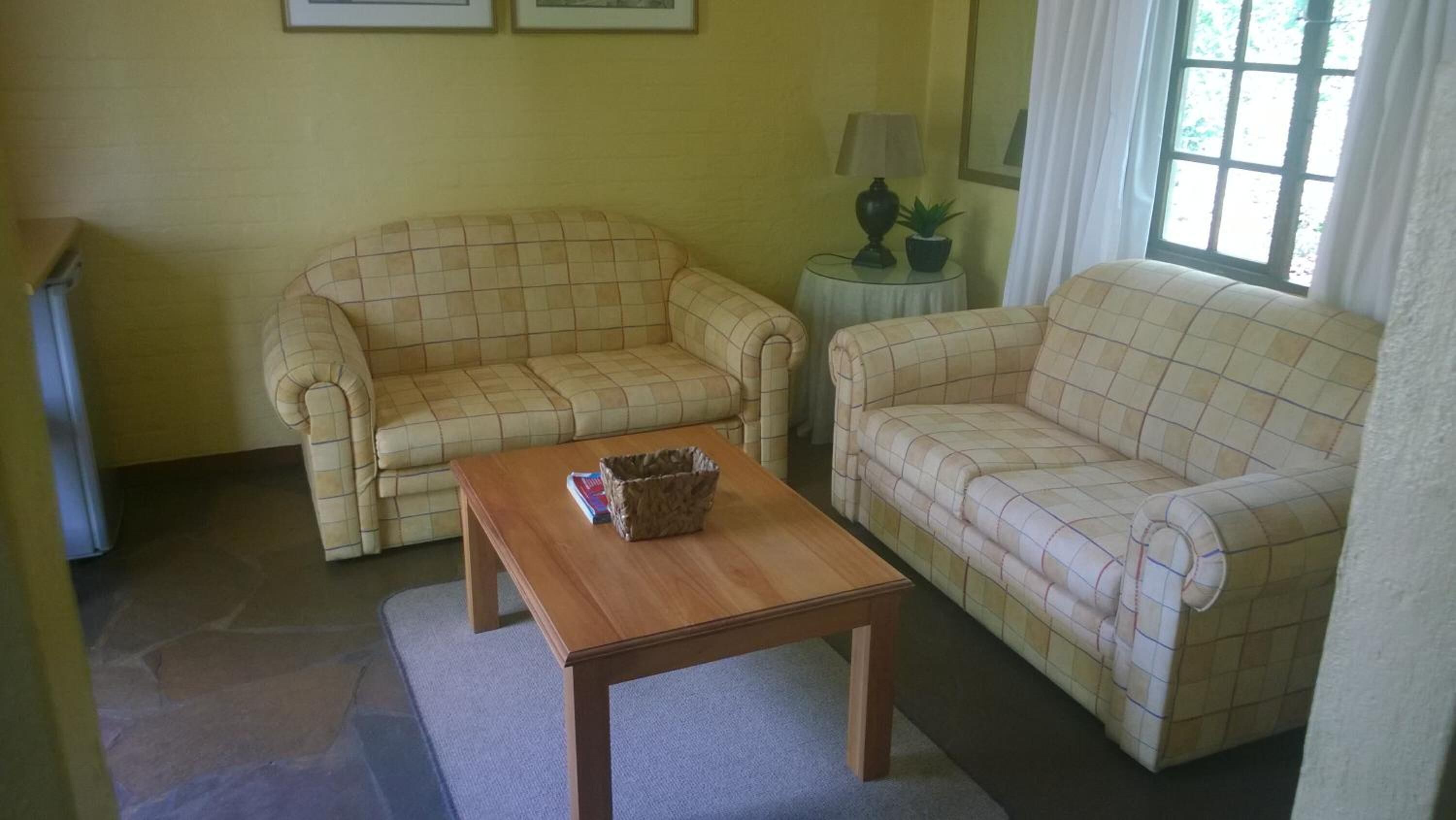A living room with two beige checkered sofas, a wooden coffee table, and a small side table with a lamp and a plant.