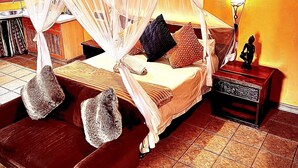Une chambre à coucher avec un lit recouvert d’une moustiquaire, une table de chevet avec une lampe et un sol carrelé.