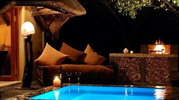 Un espace extérieur accueillant avec des sièges confortables, une piscine, un foyer et une structure dotée d’un toit de chaume.