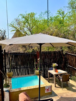A backyard with a swimming pool, a covered patio area, and a wooden fence. - Manzini Swazi King Chalets (Nkomazi)