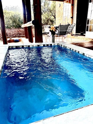 A rectangular swimming pool with clear blue water, surrounded by a tiled deck and wooden pillars. - Manzini Swazi King Chalets (Nkomazi)