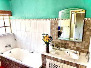 A bathroom with a bathtub, two sinks, a mirror, and a window. - Manzini Swazi King Chalets (Nkomazi)