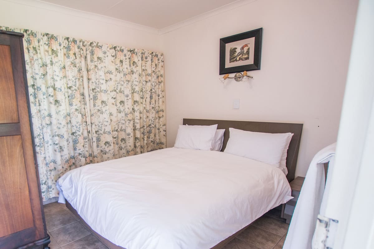 A bedroom with a bed, curtains, a framed picture, and a nightstand.